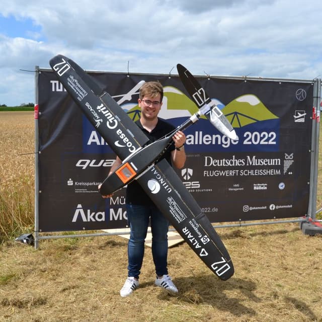 Pablo holds up CORV-0, a black carbon-fibre aircraft, in front of the Air Cargo Challenge 2022 banner.