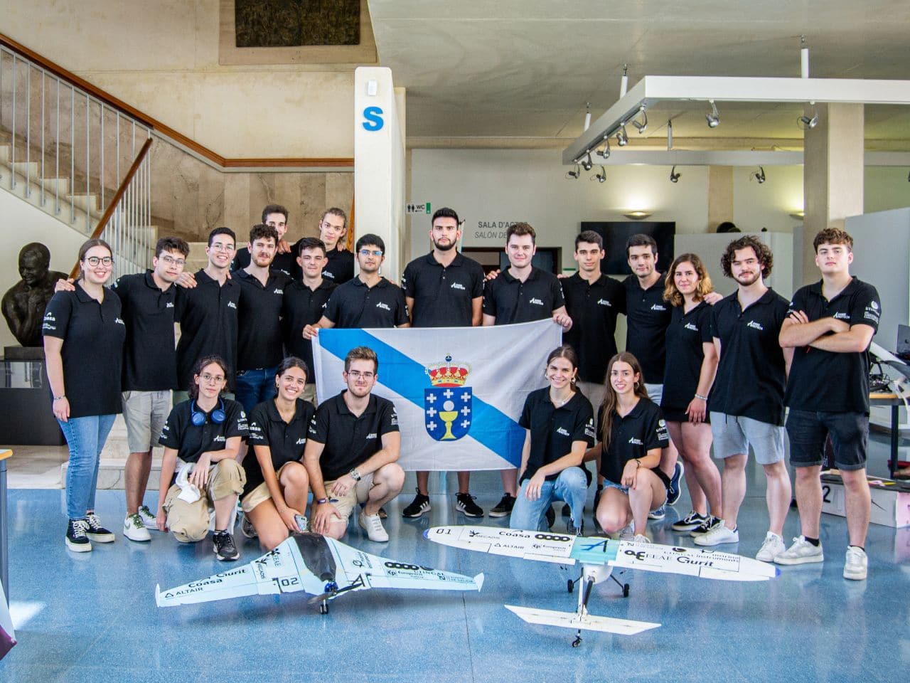 The UVigo Aerotech team, in black polo shirts and holding a Galician flag, stands behind its two aircraft, a flying wing and a conventional plane.