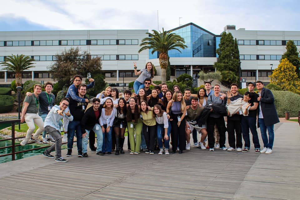 Informal group photo at the AEAE congress in Madrid, around thirty students fooling around on a wooden walkway in front of a university building.
