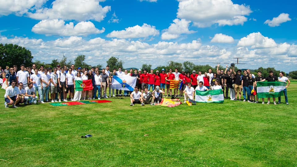 Group photo on an airfield lawn with the Spanish and Portuguese teams at the Air Cargo Challenge 2024, holding the flags of Portugal, Galicia, Spain and Andalusia.